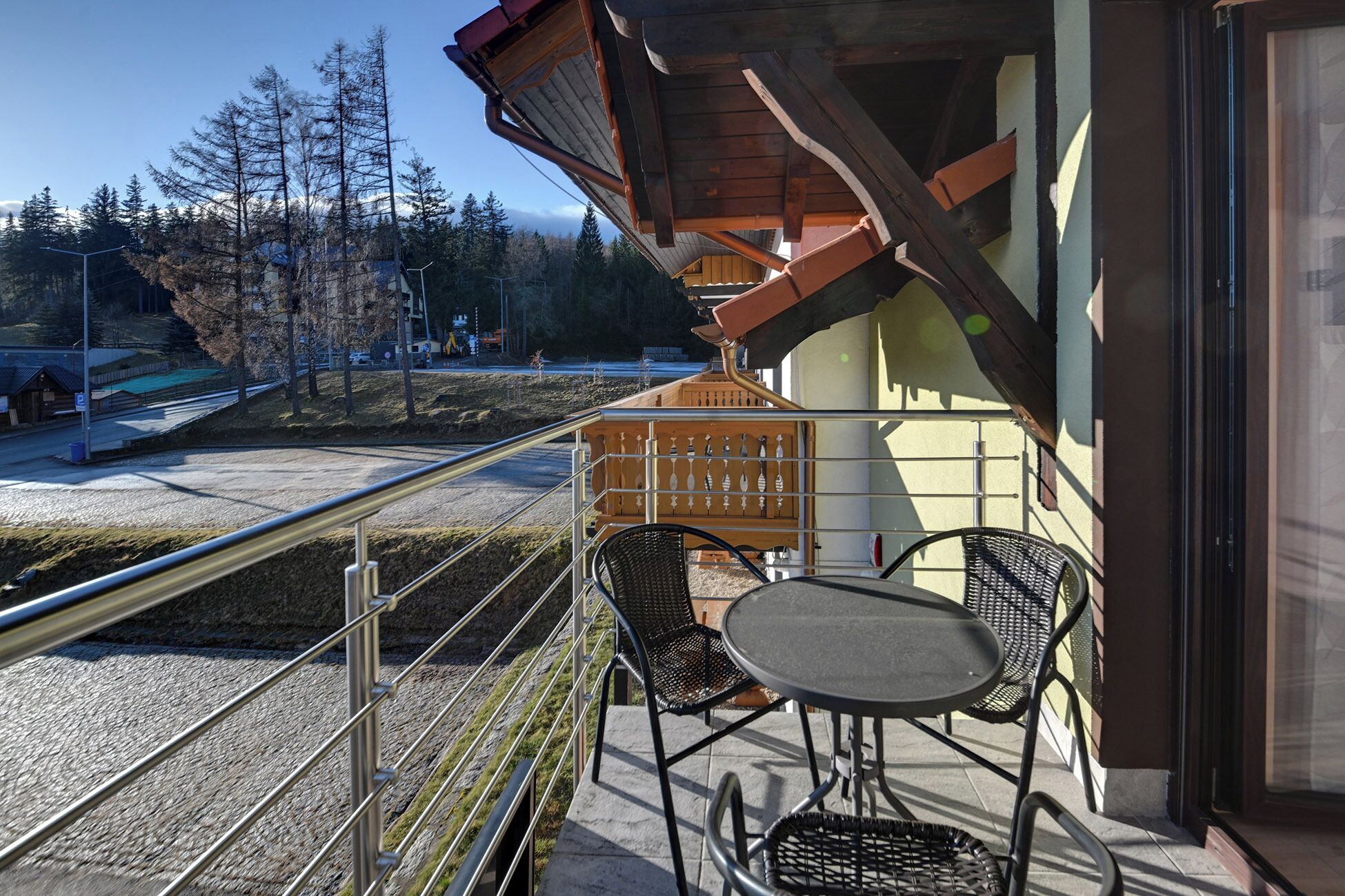 A balcony with a table and chairs, overlooking a snowy landscape and a road with vehicles.