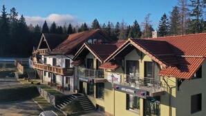 A row of traditional wooden buildings with red-tiled roofs, a ski shop, and a restaurant. - RentPlanet - Apartamenty przy Wyciągu (Szklarska Poręba)