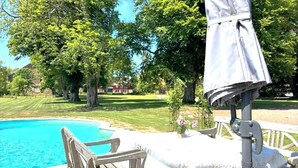Een zwembadterras met een houten stoel, een tafel met een witte tafelkleed en een parasol.