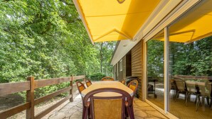 Un patio exterior con una mesa y sillas de madera, un paraguas amarillo y un suelo de baldosas de piedra.
