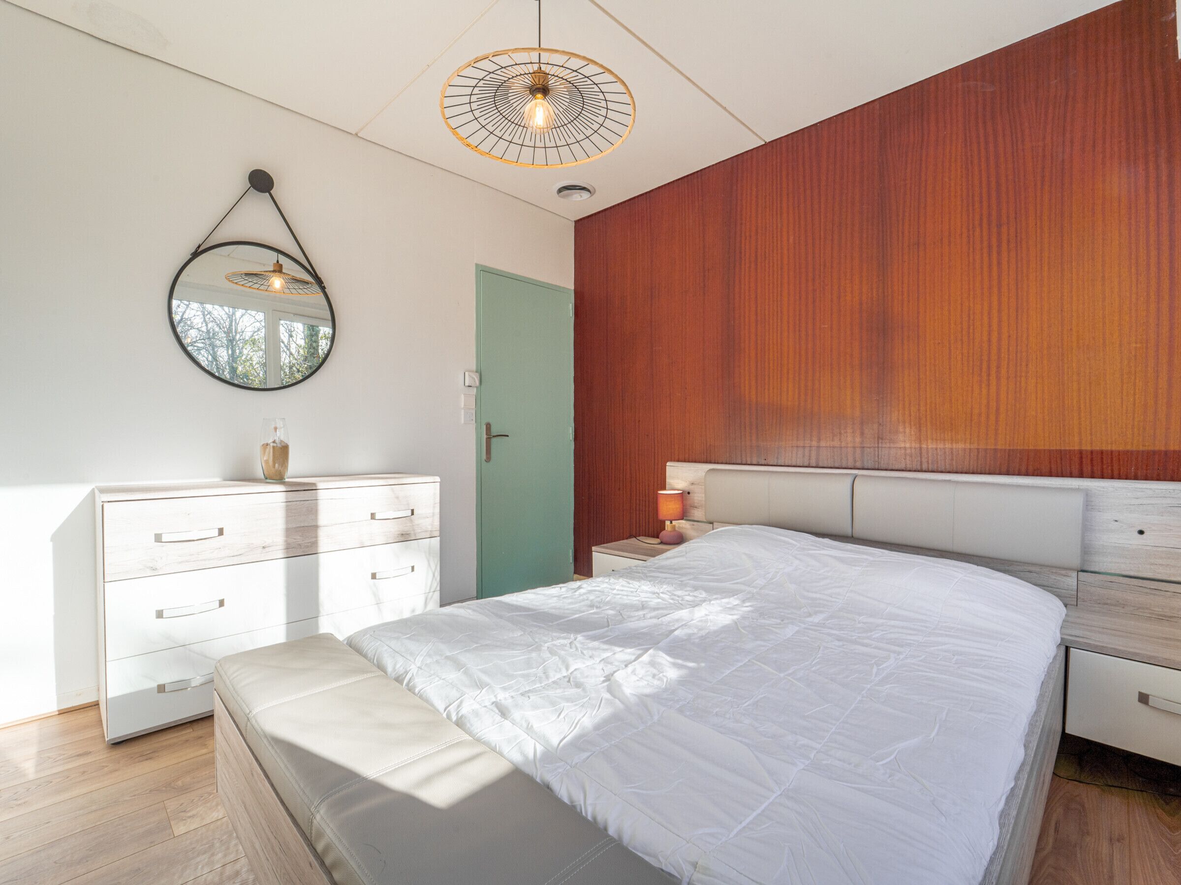 A bedroom with a bed, a dresser, a mirror, a door, and a wall-mounted light fixture.