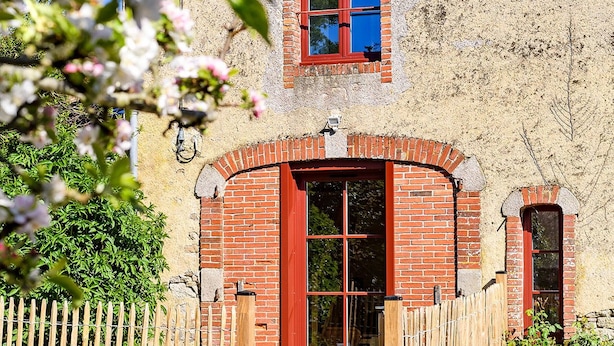 Un bâtiment rustique à la façade en briques rouges, avec une clôture en bois et un ciel bleu clair qui se reflète dans les fenêtres.