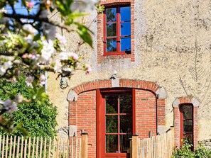 Ein rustikales Gebäude mit roter Backsteinfassade, einem Holzzaun und blauem Himmel, der sich in den Fenstern spiegelt.