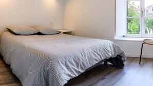 Une chambre à coucher avec un lit, deux oreillers, une table de chevet, une chaise et une fenêtre donnant sur un paysage verdoyant.