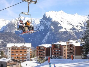 A ski lift with skiers, a mountain backdrop, and buildings with balconies. - Lovely 1-bedroom apartment, mountain corner, balcony, pets allowed (Morillon Village)