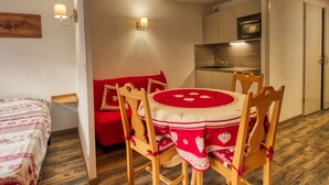 A compact room with a dining table, chairs, a sofa, and a kitchenette. - Lovely 1-bedroom apartment, mountain corner, balcony, pets allowed (Morillon Village)