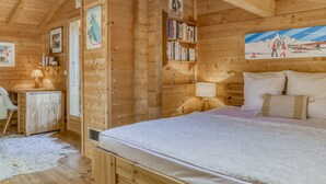 Ein gemütliches Holzblockhaus-Zimmer mit einem Bett, einem Schreibtisch und einem Bücherregal.