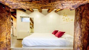 Un dormitorio con techo de madera, una cama con ropa de cama blanca y almohadas rojas, un televisor montado en la pared y un radiador.