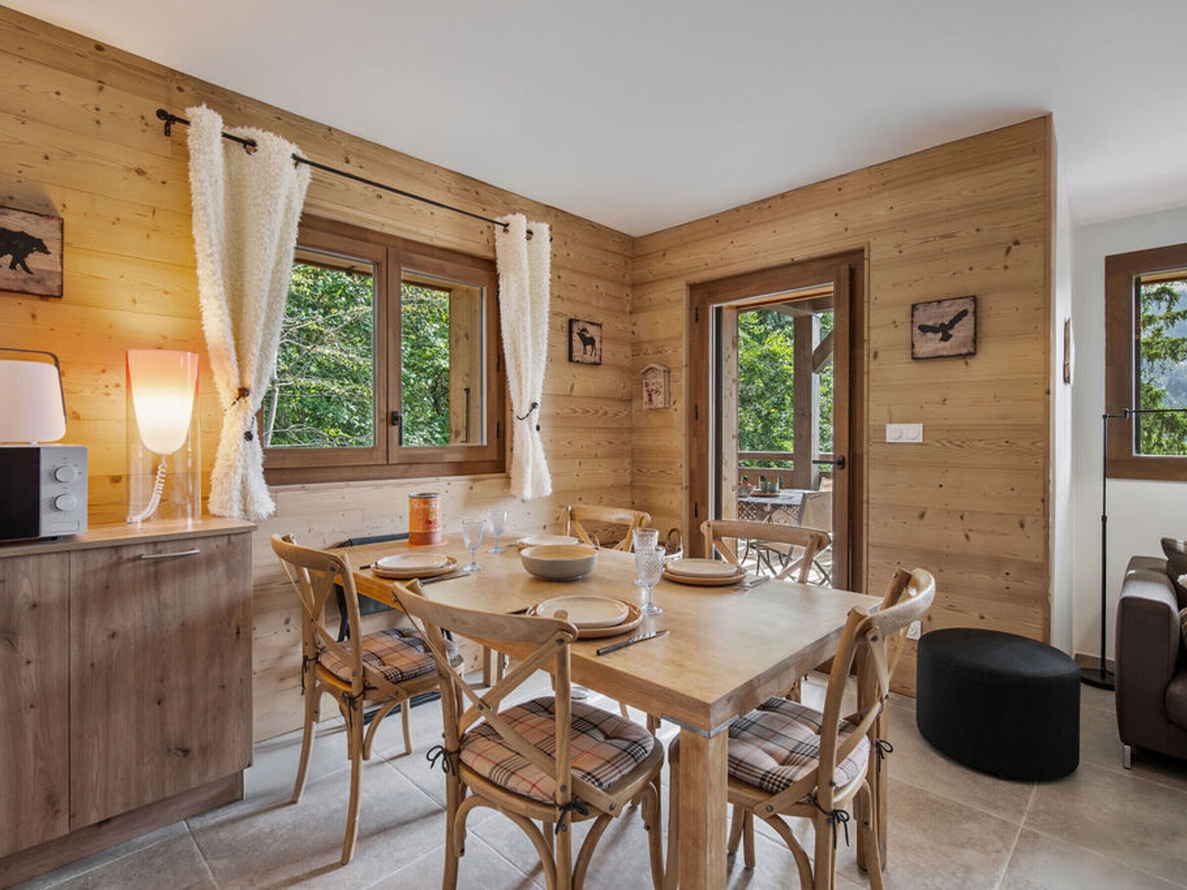 A wooden interior with a dining table set for six, surrounded by plaid chairs.