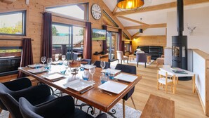 A cozy cabin interior with a dining area, a sofa, a fireplace, and a large window. - Chalet with panoramic view - 10 guests (Crest-Voland)