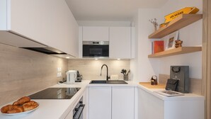 Een moderne keuken met witte kasten, een roestvrijstalen oven, een zwarte spoelbak en een aanrecht met croissants.