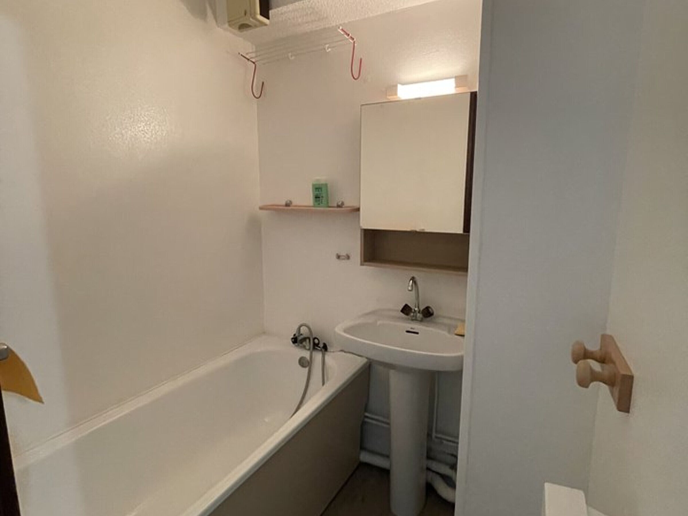 A bathroom with a bathtub, a sink, and a mirror. There are shelves above the sink and a towel rack above the bathtub.