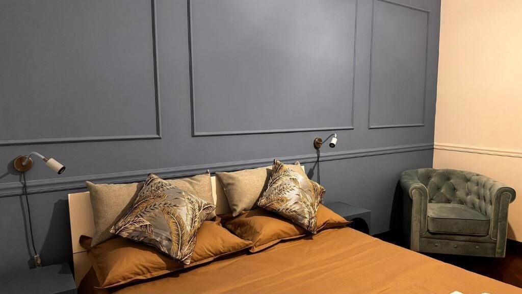 A bedroom with a bed, pillows, a nightstand, a lamp, and a chair.