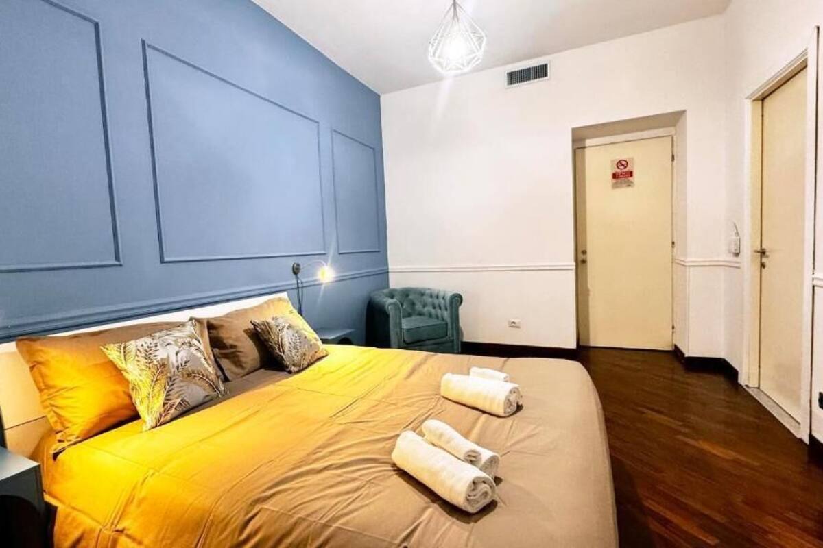 A hotel room with a bed, a chair, a door, and a light fixture.
