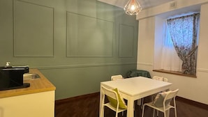 A small kitchenette with a sink and a coffee maker, a white dining table with four chairs, and a window with a floral curtain. - Raffy in Rome (Rome)