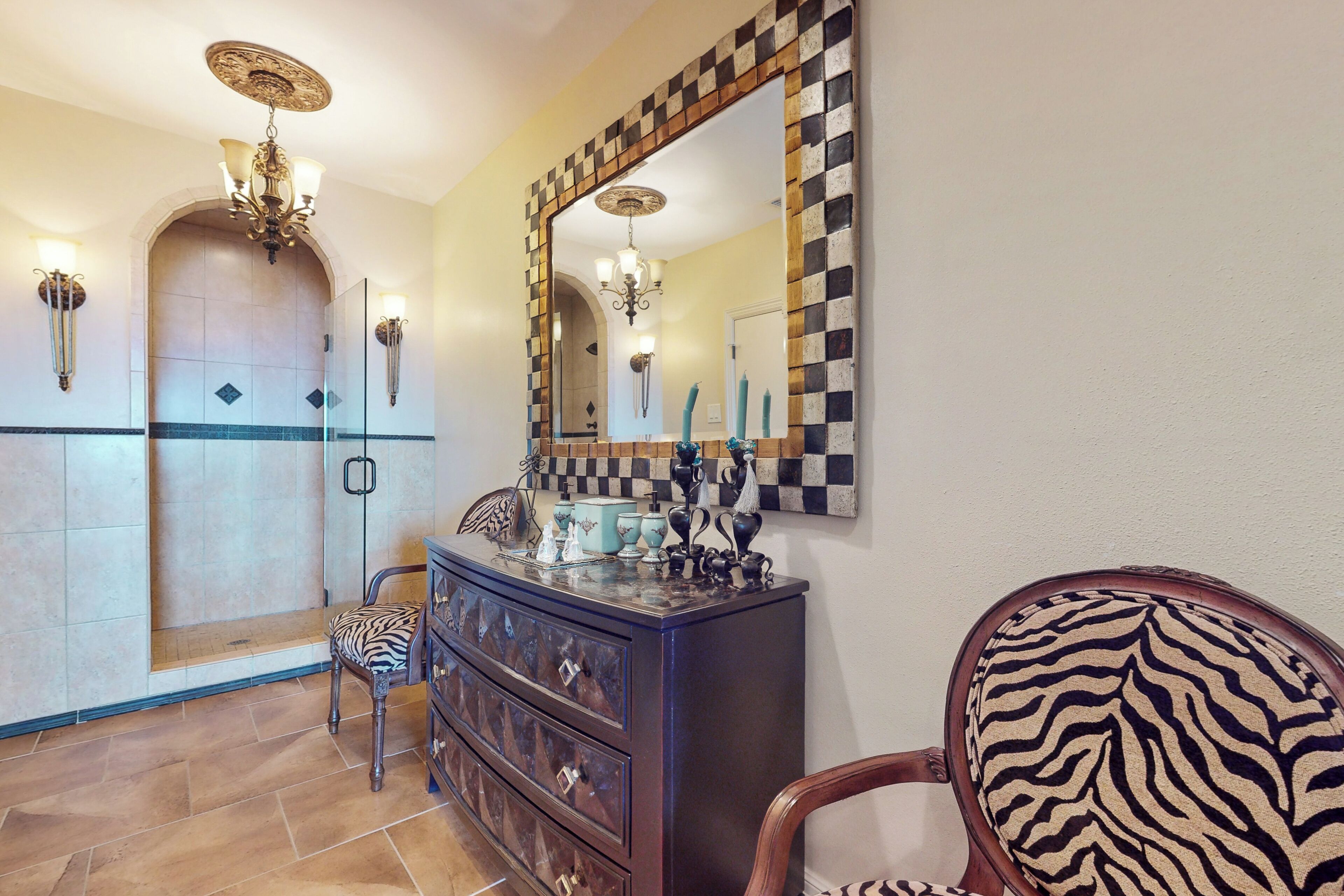 A bathroom with a checkered mirror, a zebra-patterned chair, and a wooden vanity with drawers.