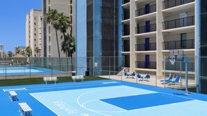 A basketball court with a fence, benches, and lounge chairs.