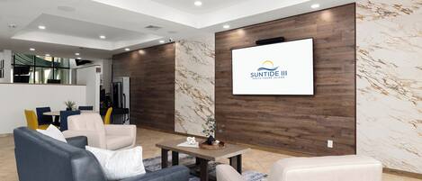 Ein modernes Wohnzimmer mit Sofa, Sesseln, Couchtisch und einem Fernseher, der ein Logo zeigt.