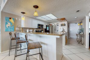 Une cuisine moderne dotée d’un îlot central, de tabourets de bar, de luminaires suspendus et d’un élément décoratif mural.