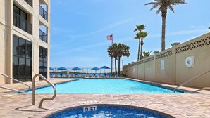 A swimming pool with a 3 FT depth marker, surrounded by lounge chairs and umbrellas, with a palm tree and American flag in the background. - Gorgeous 3BR Penthouse w/ Lanai Facing the Gulf (South Padre Island)
