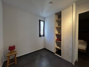 Une pièce avec une fenêtre, une petite table avec une lampe et une armoire dont les portes sont décorées de motifs.