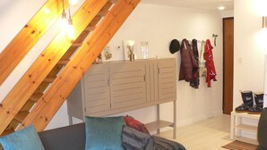 Una habitación con techo inclinado, un sofá con cojines, un armario y un perchero con chaquetas.