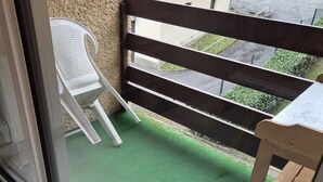 Un balcón con piso de césped artificial verde, una silla de plástico blanco y una mesa de madera.