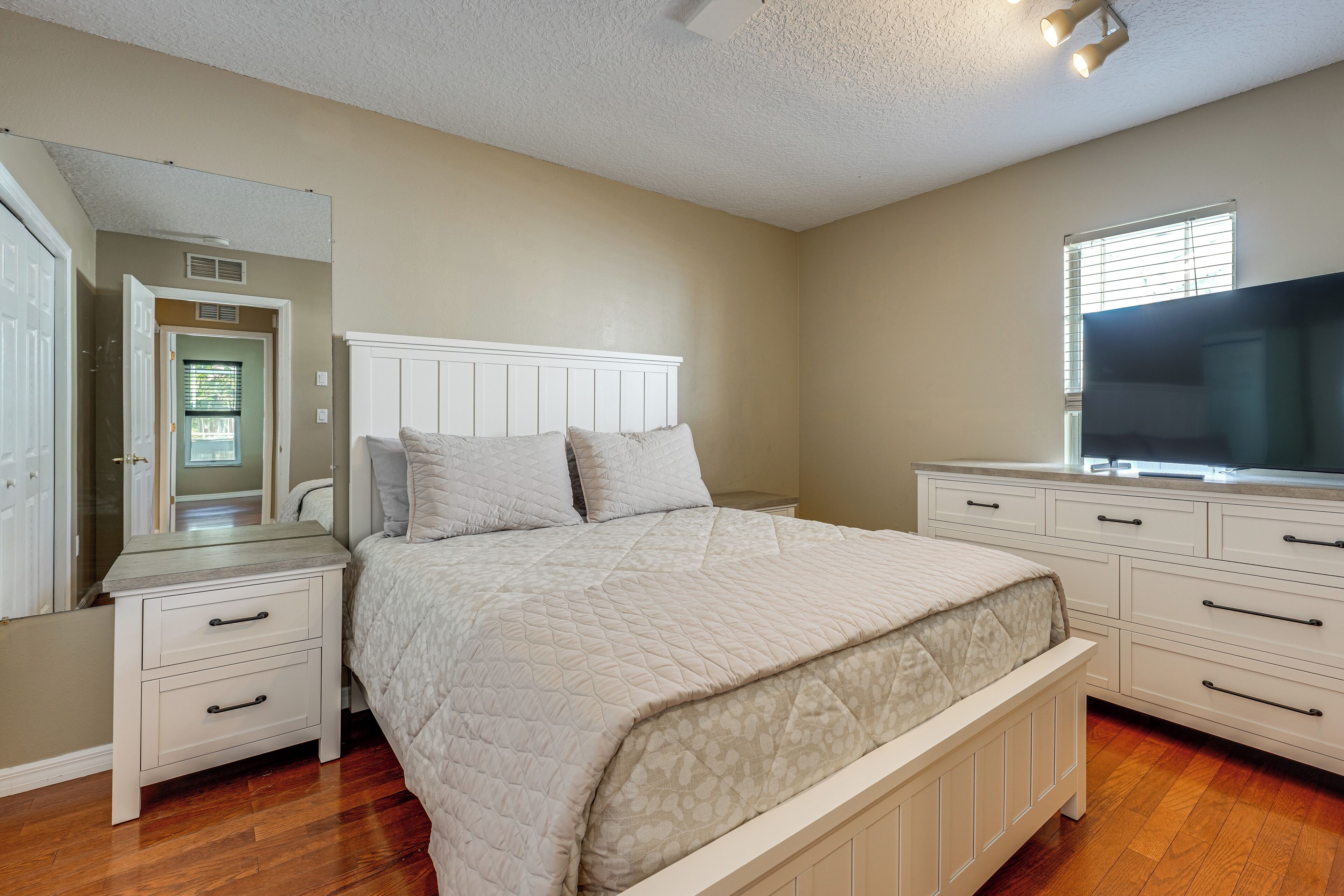 A bedroom with a bed, nightstands, a dresser, a mirror, and a television.