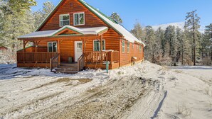 Eine Blockhütte mit Veranda und Stufen zum Eingang, umgeben von verschneiter Landschaft und Bäumen.