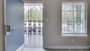 A room with a sliding glass door leading to a balcony, a window with blinds, and a door with a keypad lock. - Courtyard + Gym Access: Queen City Convenience! (Charlotte)