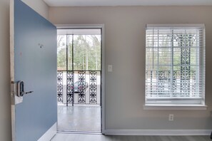 A room with a sliding glass door leading to a balcony, a window with blinds, and a door with a keypad lock. - Courtyard + Gym Access: Queen City Convenience! (Charlotte)