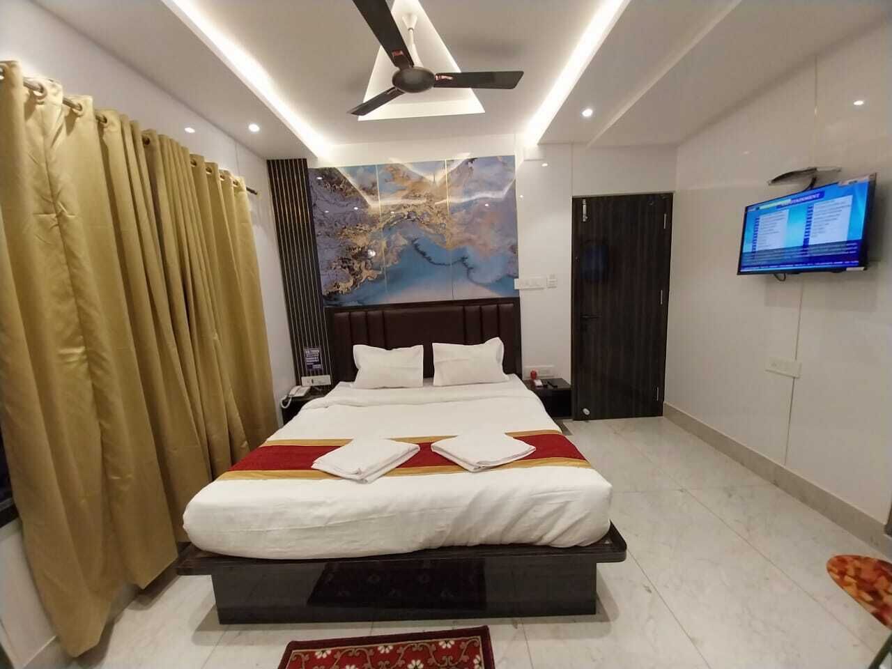 A hotel room with a large bed, a ceiling fan, a flat-screen TV, and a large window with curtains.