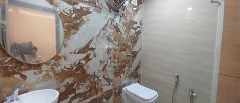 Egy márványburkolatú falú fürdőszoba, mosdókagylóval, WC-vel és zuhanyzóval.