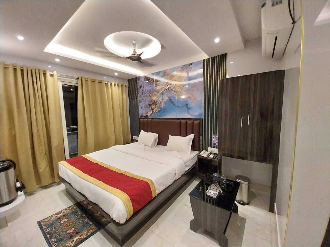 A modern hotel room with a large bed, a desk, a mirror, and a painting on the wall.