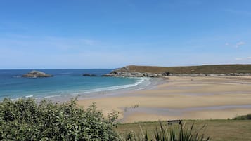 A beach with clear skies, calm waters, and distant hills.