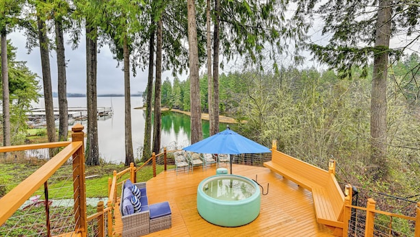 Une terrasse en bois avec un jacuzzi, du mobilier d’extérieur et une vue sur un lac et une forêt.