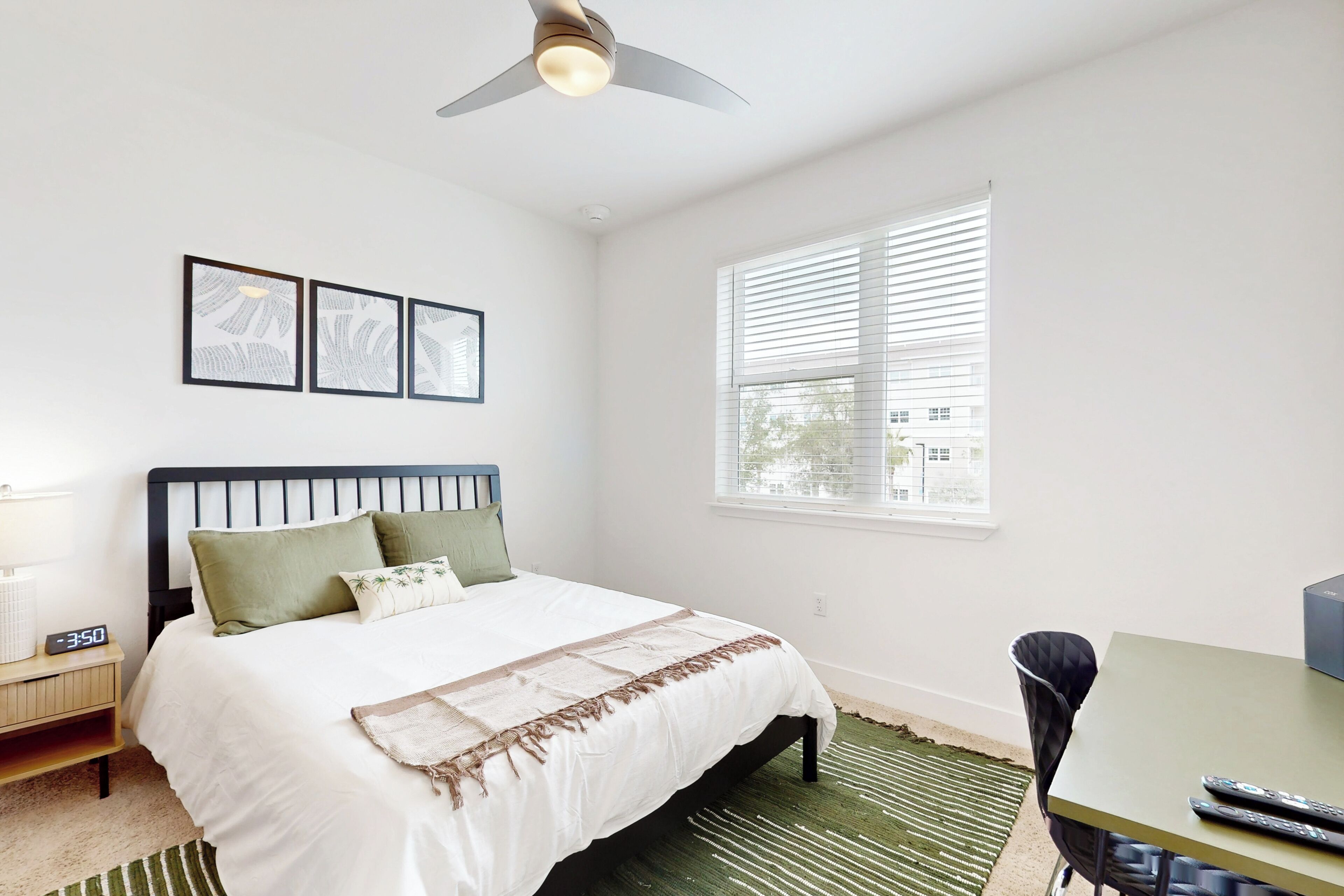 Une chambre à coucher avec un lit, une table de chevet, un bureau et une fenêtre avec des stores.