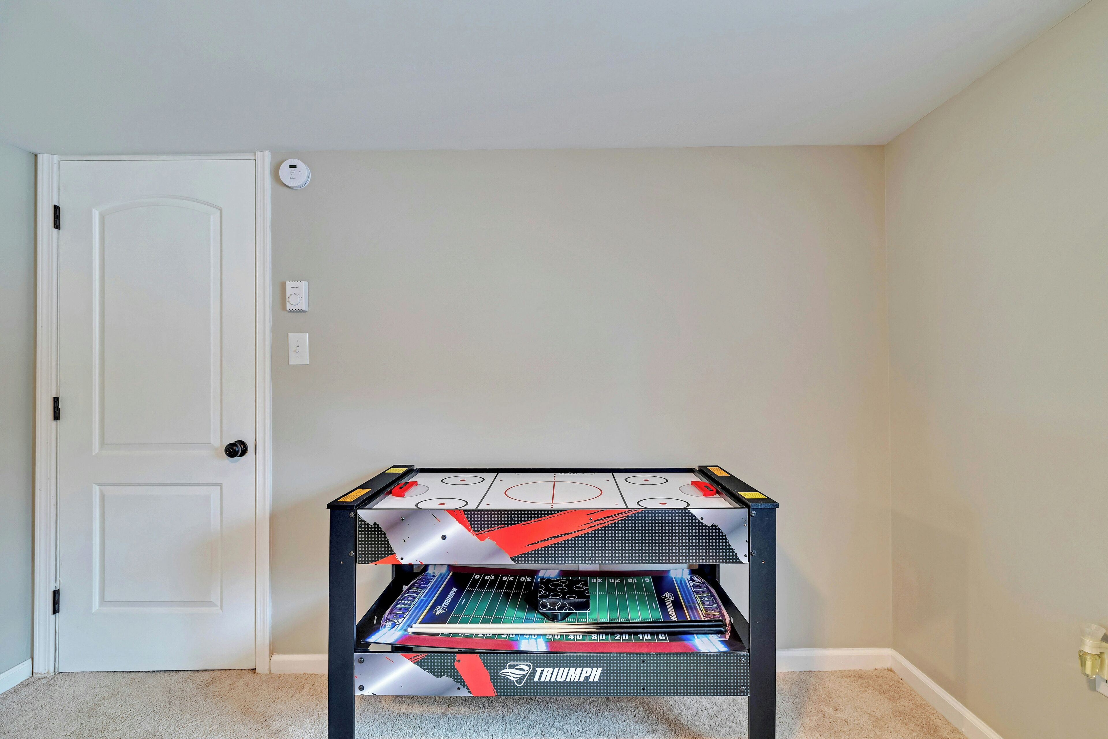 Quarto com porta branca, termostato e mesa de jogos Triumph.