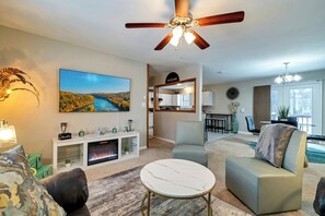 A modern living room with a fireplace, a ceiling fan, and a large TV. - Pool Access! All-season Family Home in Poconos (Long Pond)