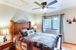 A bedroom with a wooden bed, a ceiling fan, a nightstand with a lamp, and a window with curtains. - White Mountains Cabin: Near Trails & Lake Access! (Show Low)