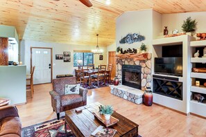 A spacious living area with a stone fireplace, wooden ceiling, and a dining area with a table and chairs. - White Mountains Cabin: Near Trails & Lake Access! (Show Low)