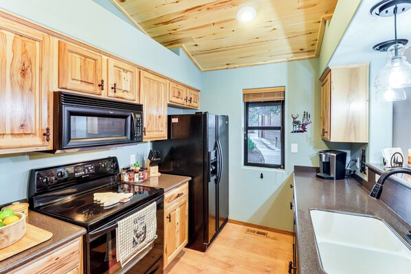 A kitchen with wooden cabinets, a black stove, a refrigerator, and a window with blinds. - White Mountains Cabin: Near Trails & Lake Access! (Show Low)
