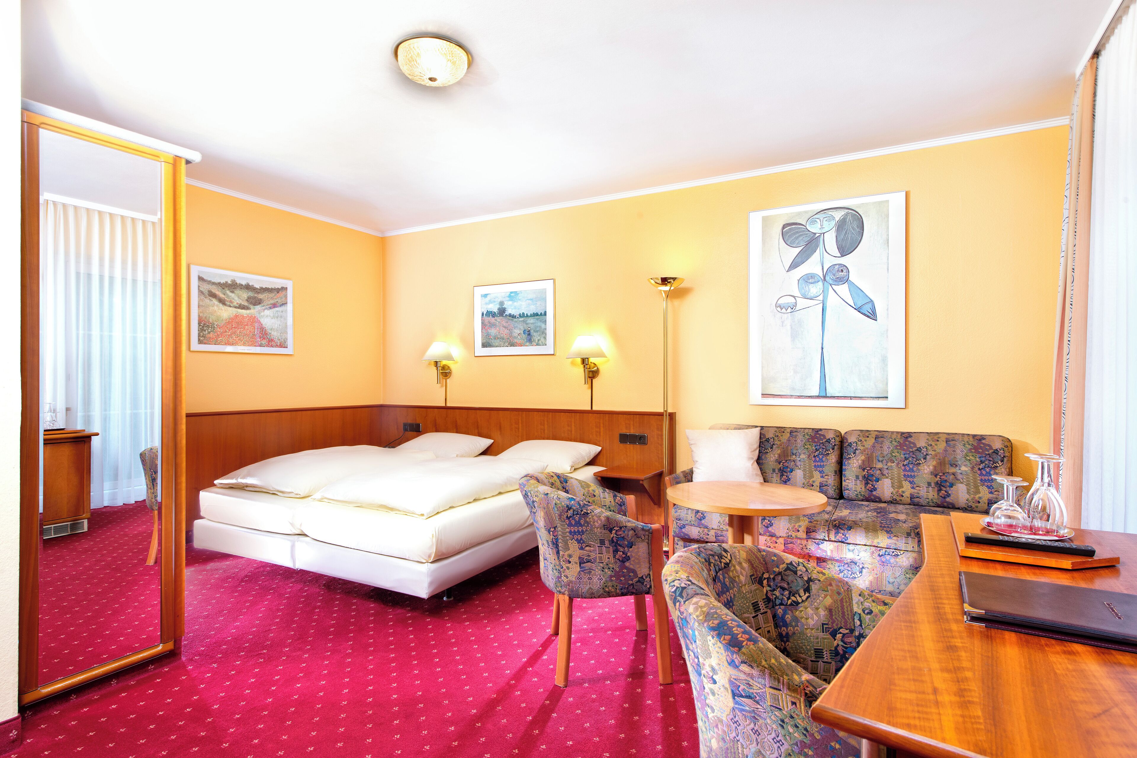 Una habitación de hotel con cama, sofá, sillón, mesita y espejo.