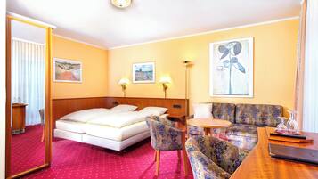 Una habitación de hotel con cama, sofá, sillón, mesita y espejo.