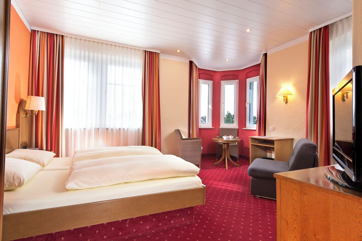 Una habitación de hotel con una cama grande, un escritorio, una silla, un televisor y una pequeña mesa.
