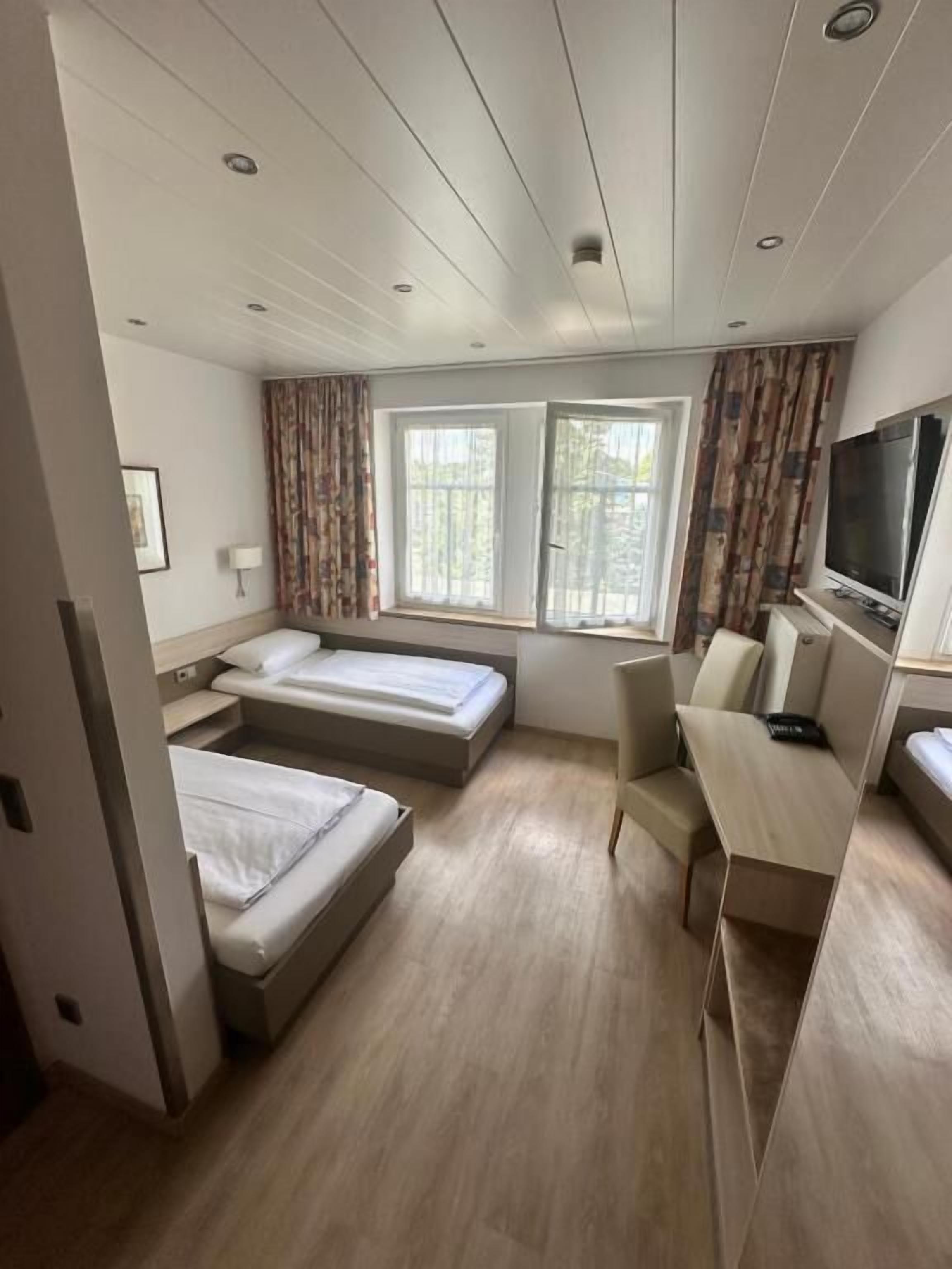 Ein kompaktes Hotelzimmer mit zwei Einzelbetten, einem Schreibtisch mit Fernseher und zwei mit Vorhängen versehenen Fenstern.
