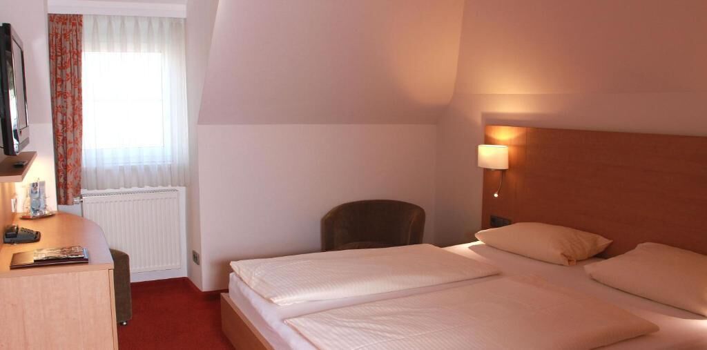A hotel room with two beds, a desk with a computer, a chair, and a window with curtains.