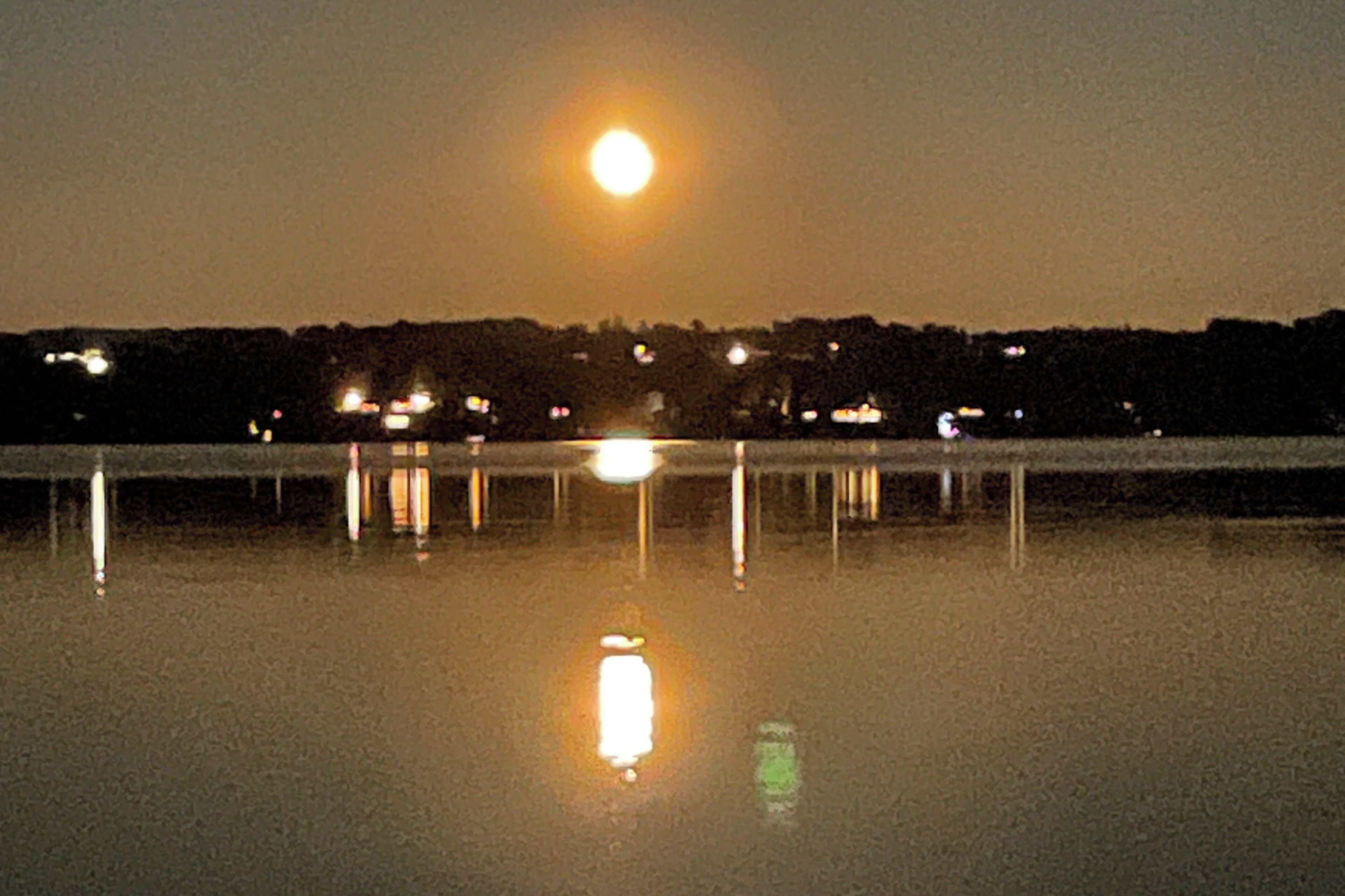 A nighttime view of a body of water with a full moon reflecting on the surface.
