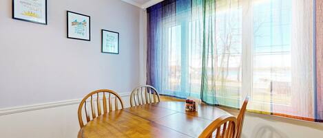 A dining area with a wooden table and chairs, framed motivational quotes on the wall, and a large window with colorful curtains.