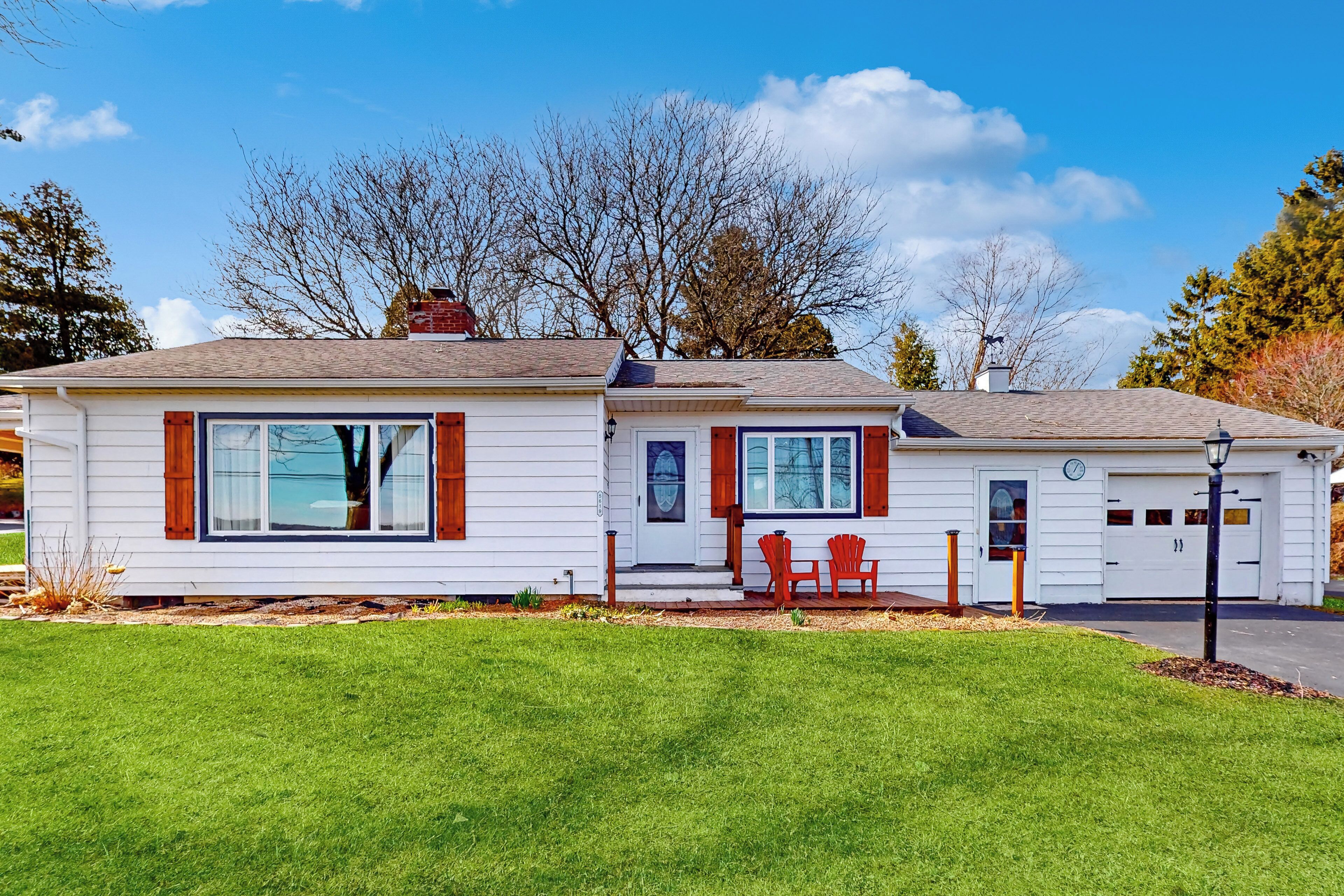 A two-story house with a garage, a front porch with red chairs, and a well-maintained lawn.